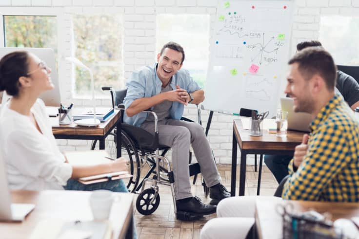 Office workers and man in a wheelchair discussing business moments in a modern office.